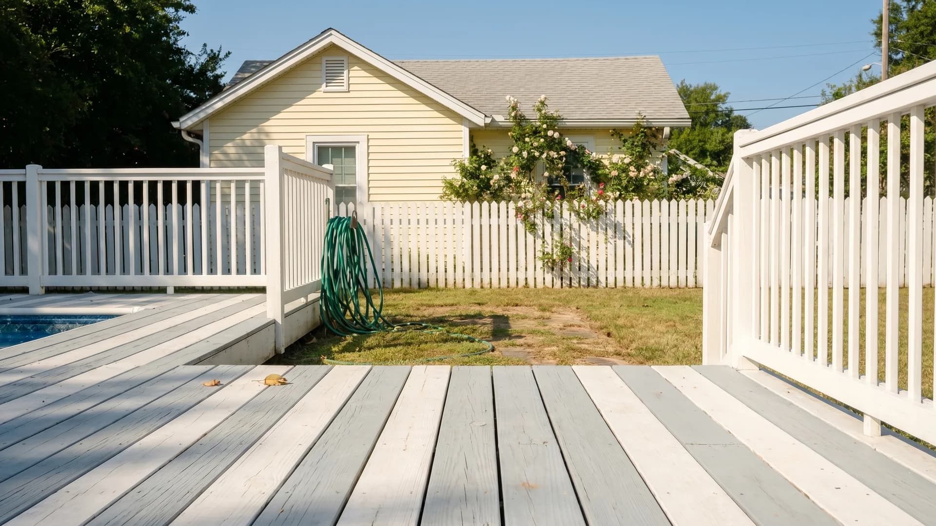 Two-tone pool deck with gray boards and white railing at a pale yellow cottage