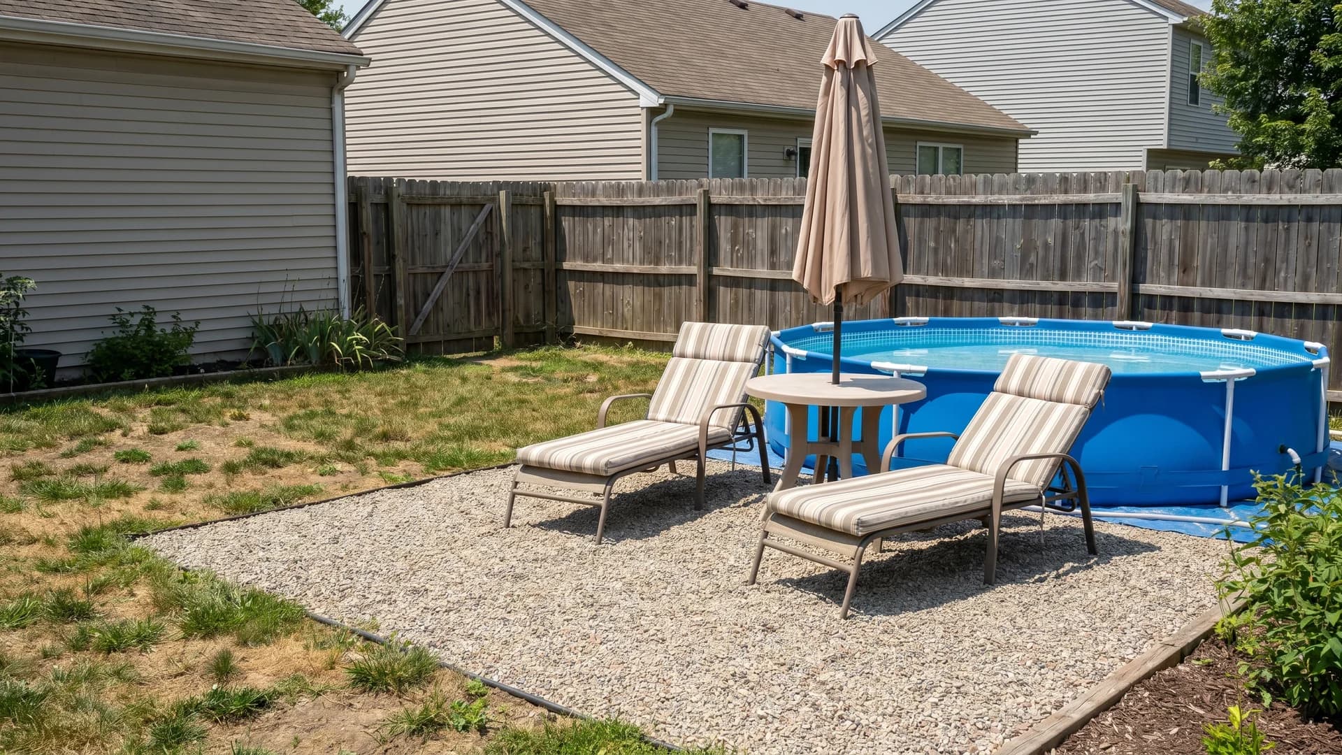 Gravel sun patio with two loungers and an umbrella next to an above ground pool