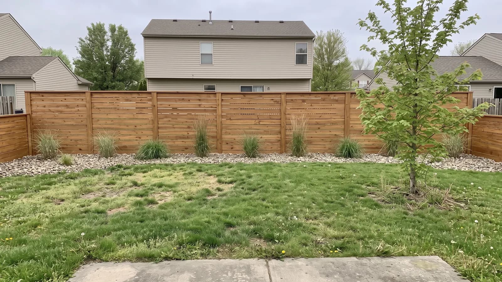 The same backyard with a six-foot horizontal cedar board fence and a gravel strip with ornamental grasses