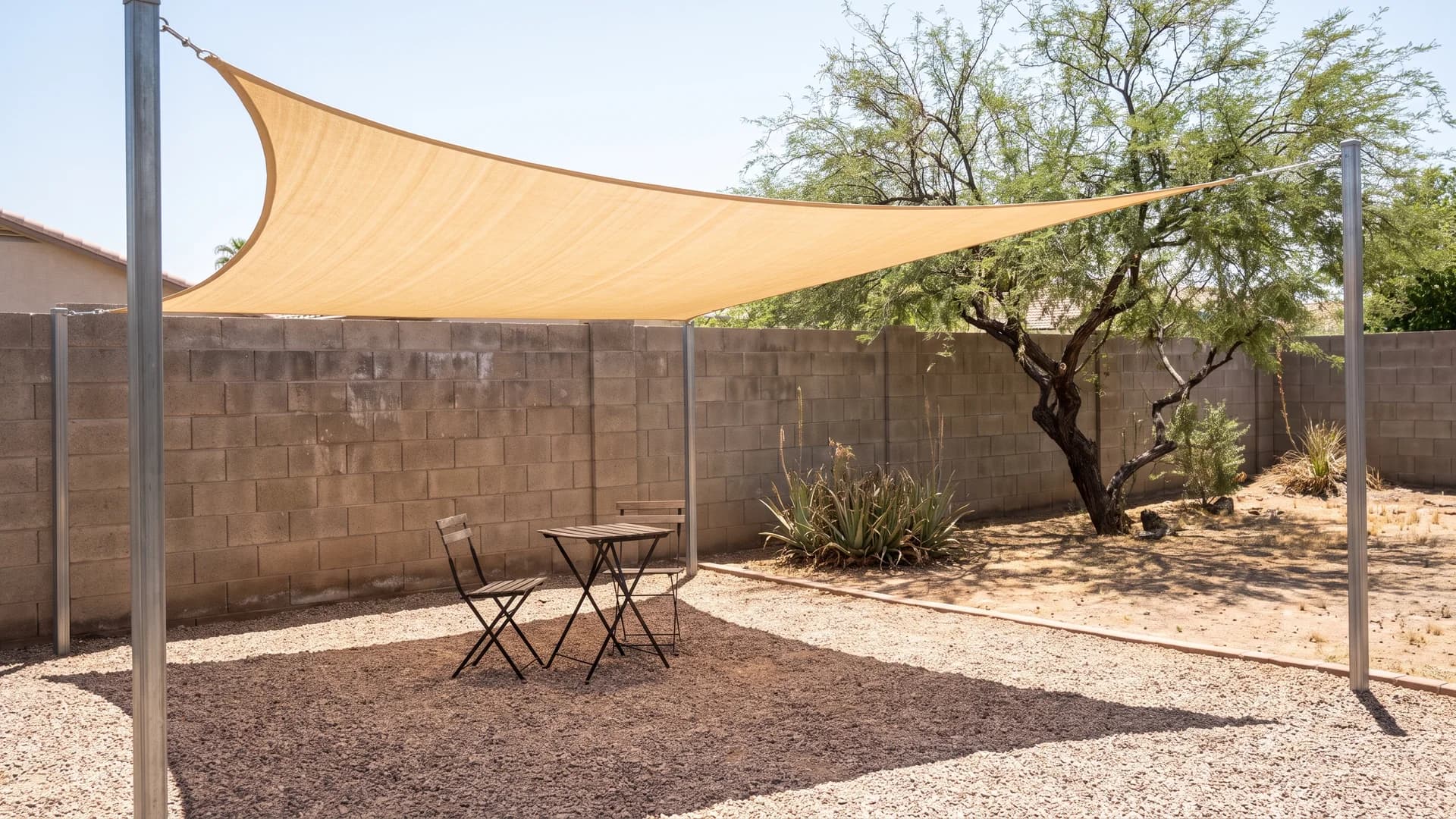 Shade sail stretched over a gravel patio and outdoor seating in a desert backyard