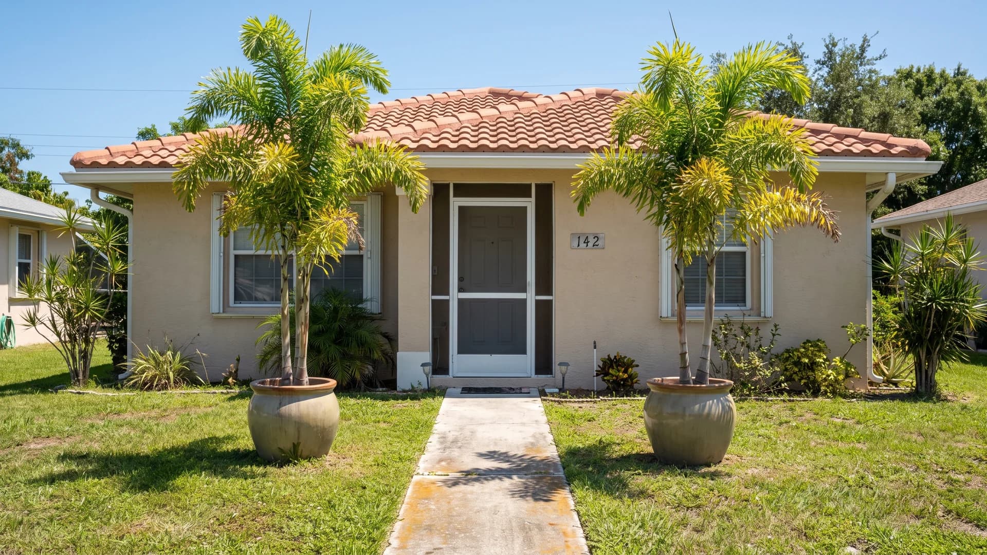 Matched foxtail palms and containers flanking the front door of a stucco home