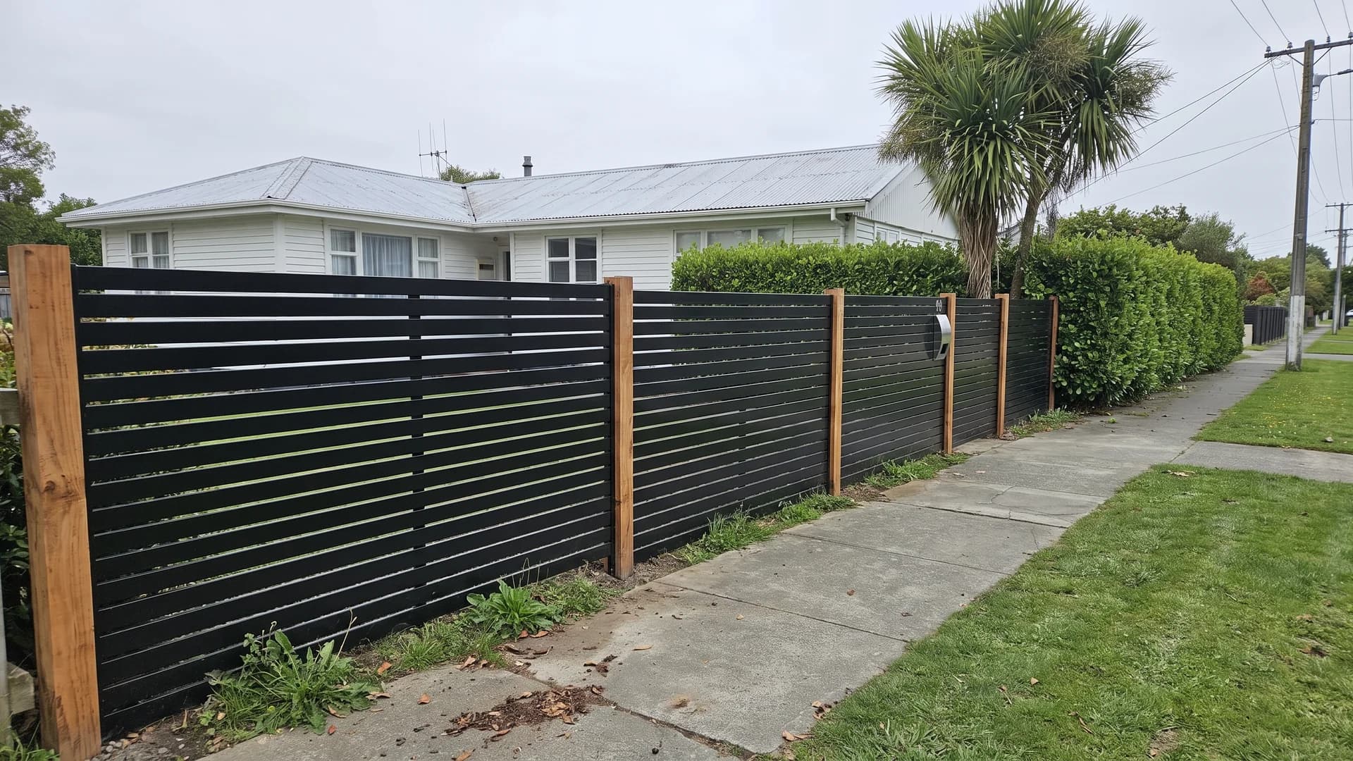 Matte black aluminium horizontal battens between raw timber posts along a street front