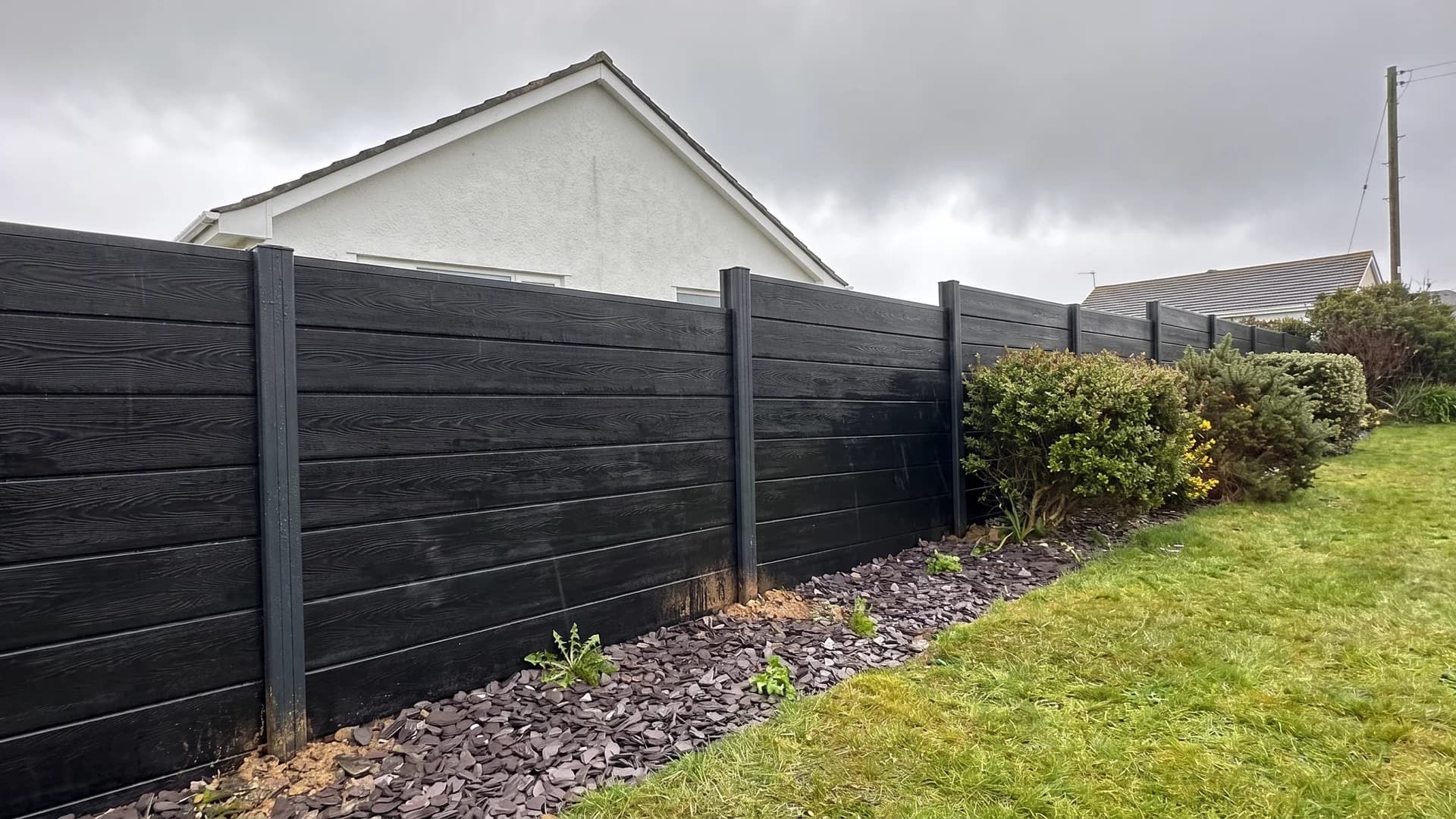 Charcoal composite boundary fence stepping down a windswept coastal garden