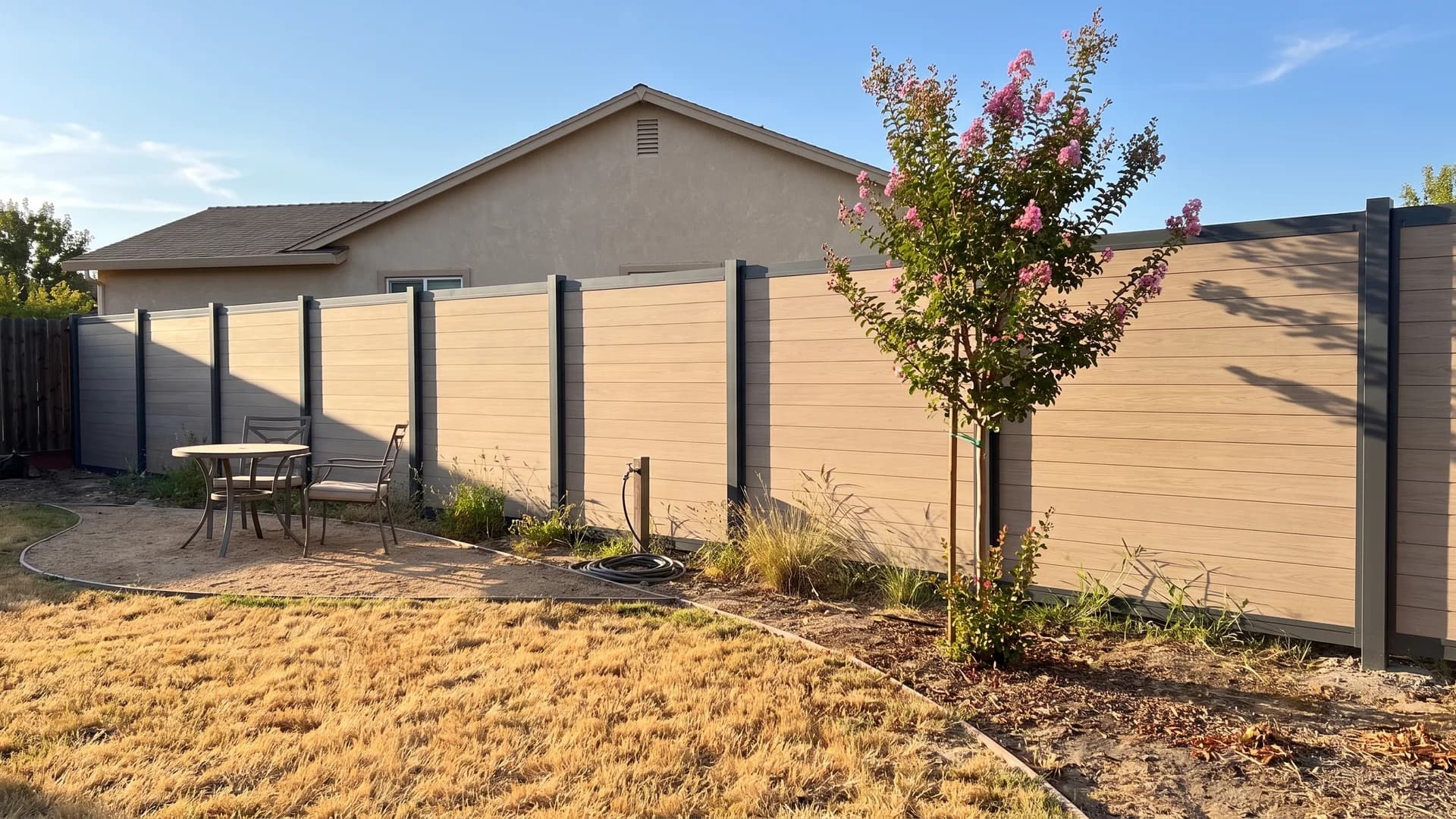 Tan composite fence boards framed by charcoal aluminium posts along a dry backyard