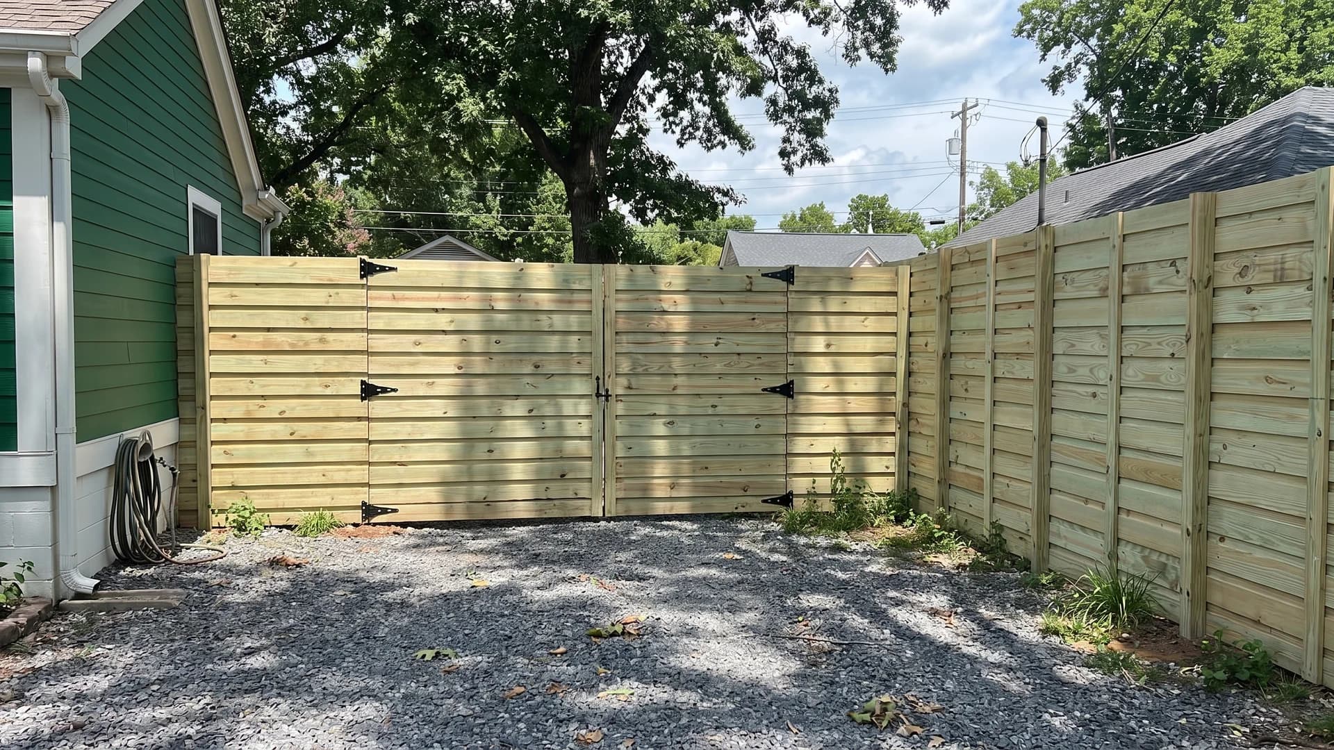 Eight-foot pressure-treated board-on-board fence with a double gate in a gravel backyard