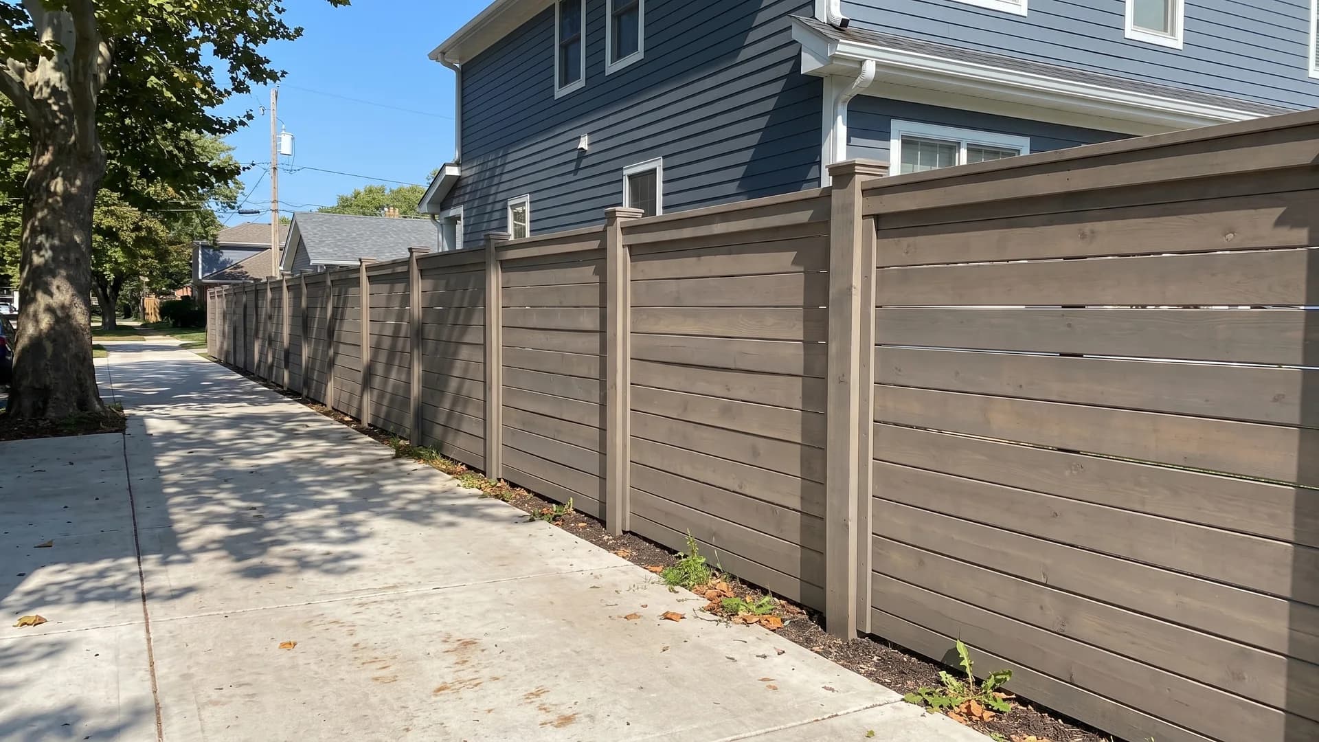 Grey-brown stained horizontal board fence with a capped top rail along a suburban driveway