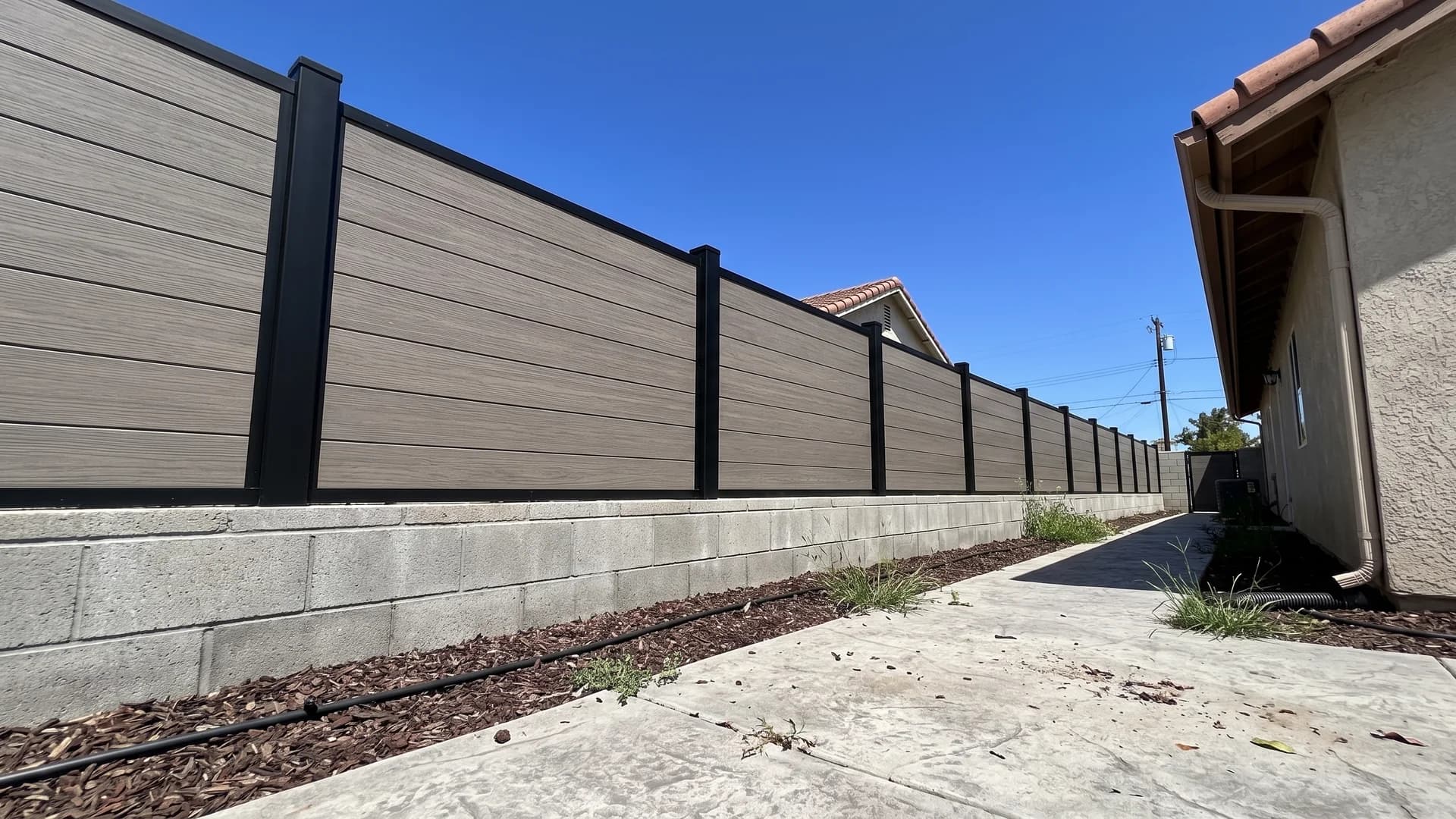 Grey-brown composite horizontal boards with black posts set above a low block wall in a side yard