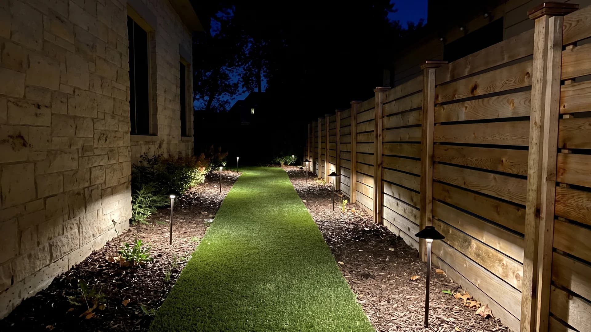 Cedar boards lit by low path lights along a narrow turf side yard at night