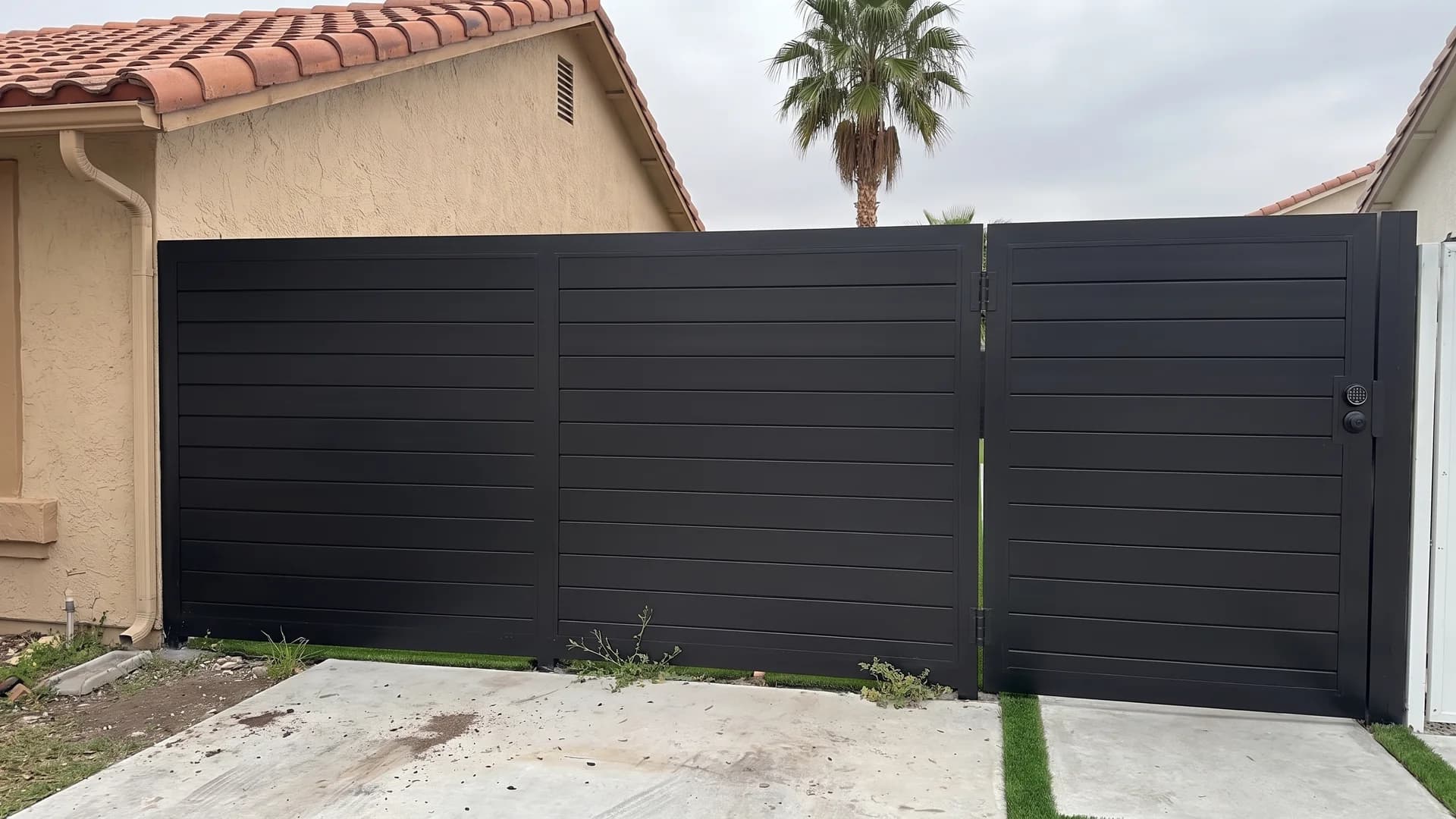 Matte black horizontal metal fence with a flush matching side gate above concrete and turf paving