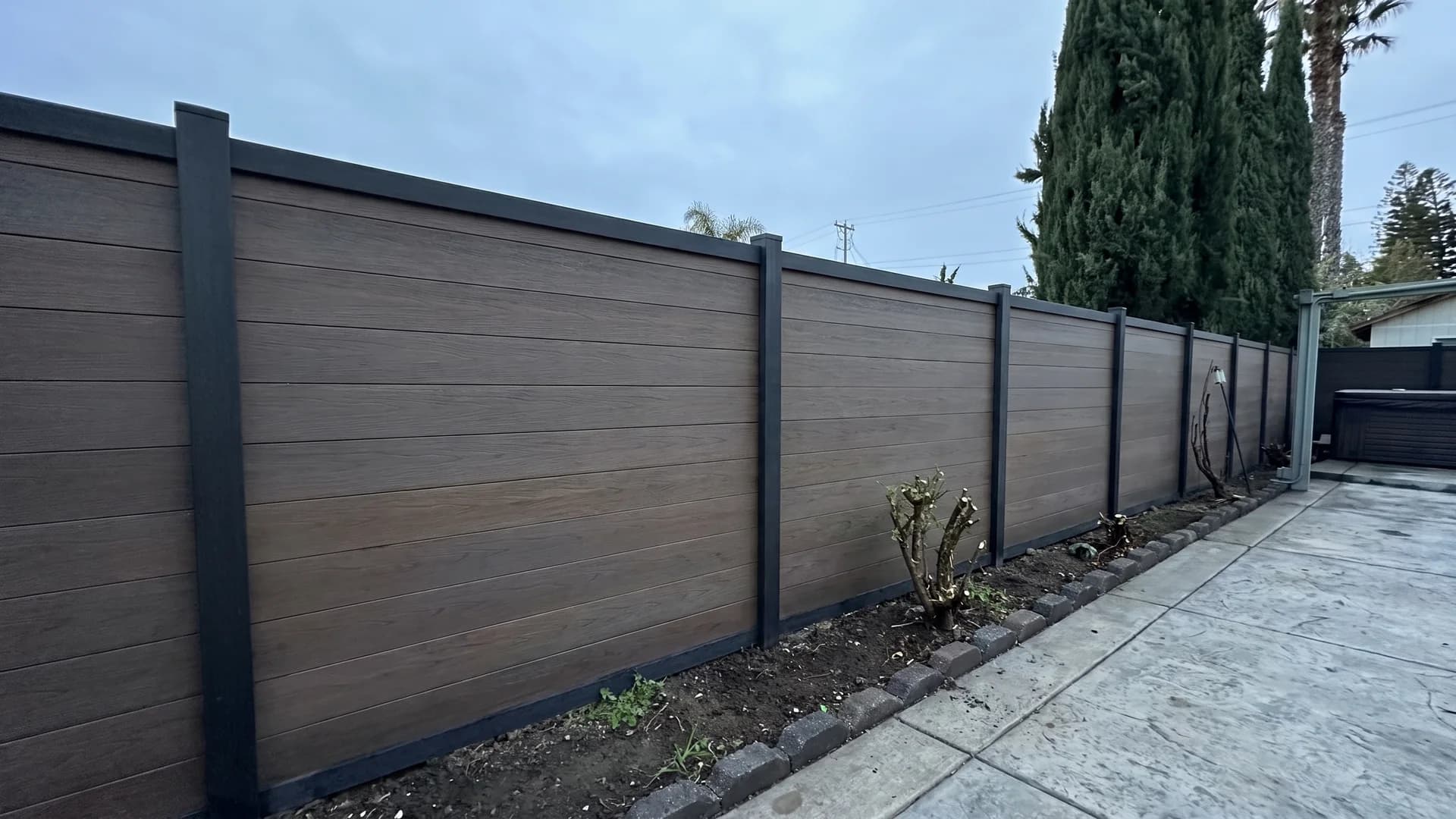 Warm walnut composite fence with charcoal posts beside a stamped concrete side yard path