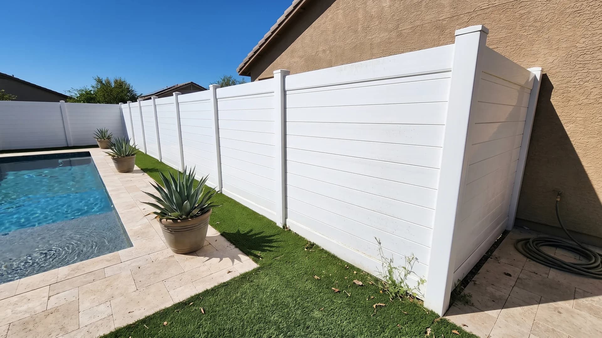 White vinyl horizontal-plank privacy fence enclosing a travertine pool deck