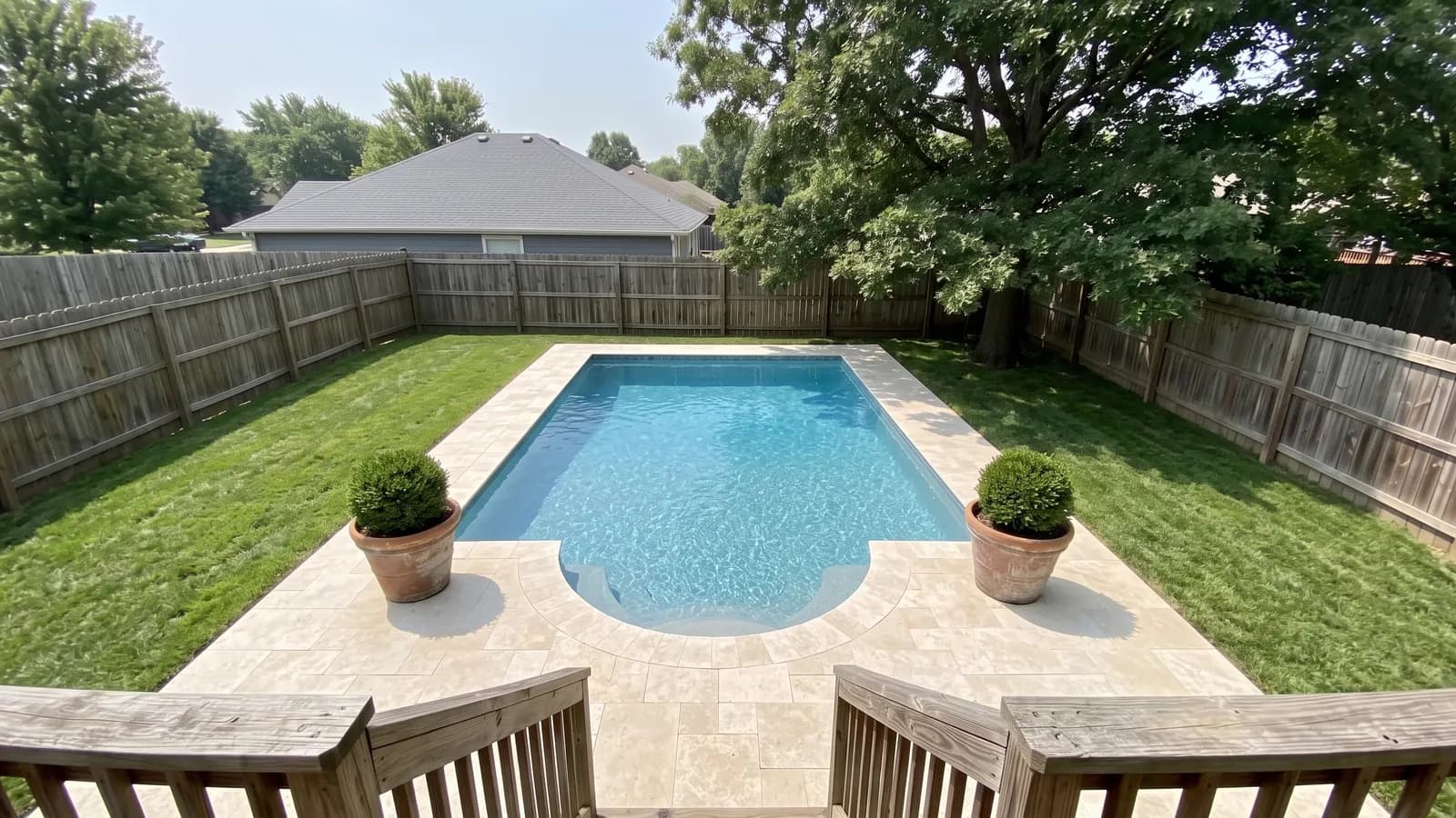 A rectangular pool with a semicircular Roman end holding curved steps, cream travertine coping and potted boxwoods