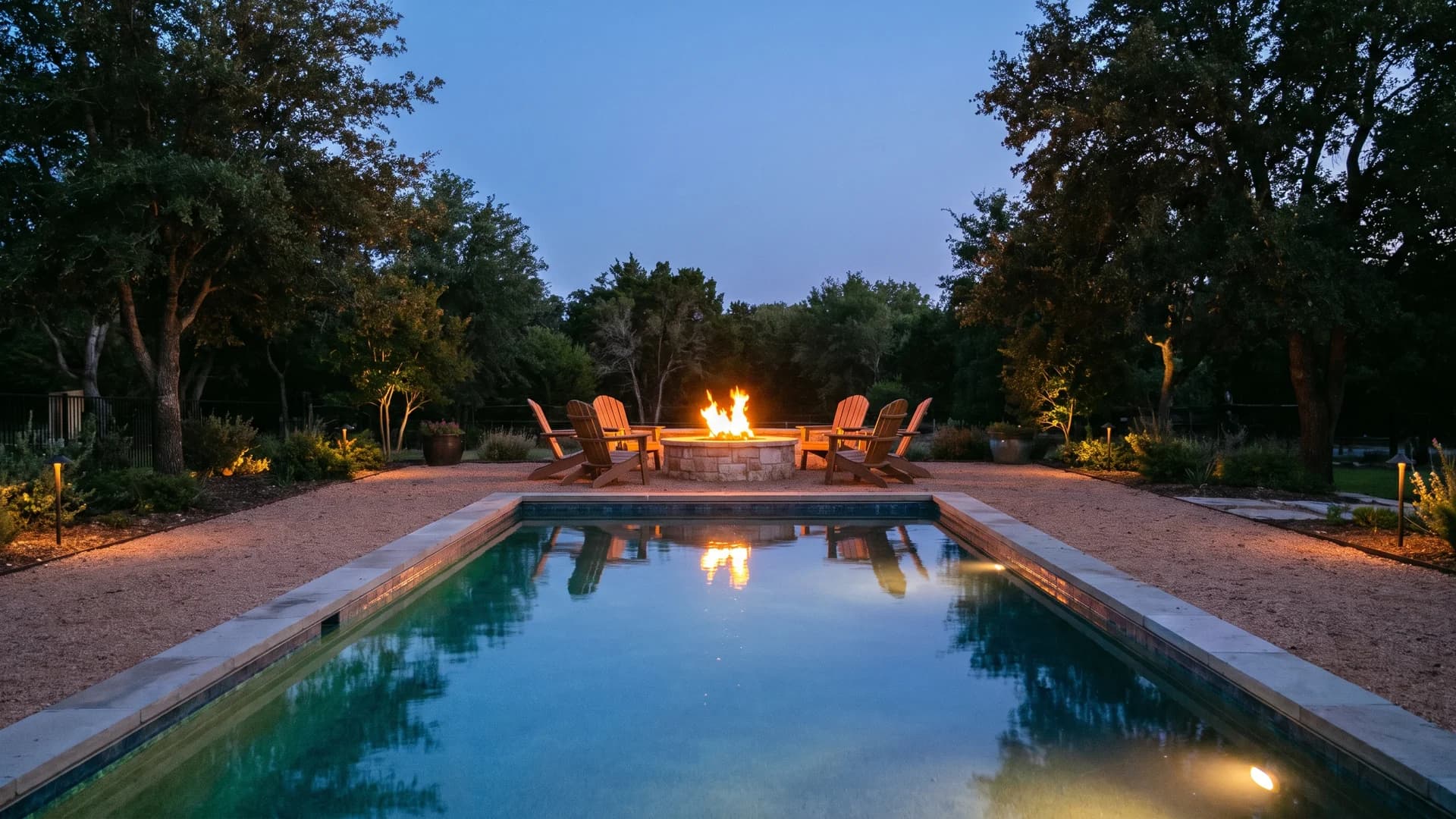 Fire pit lounge area at the far end of a rectangular pool in the evening