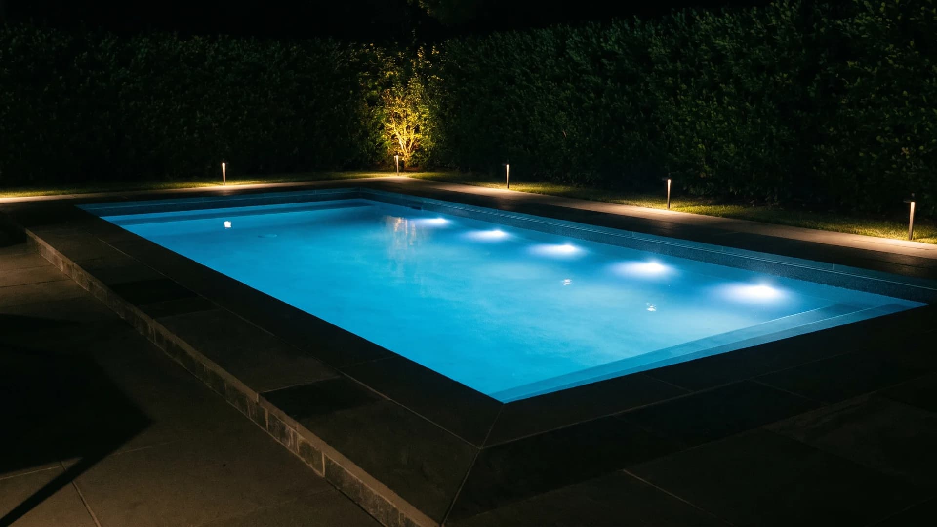 Rectangular pool at night with underwater LEDs and path lighting along its lines
